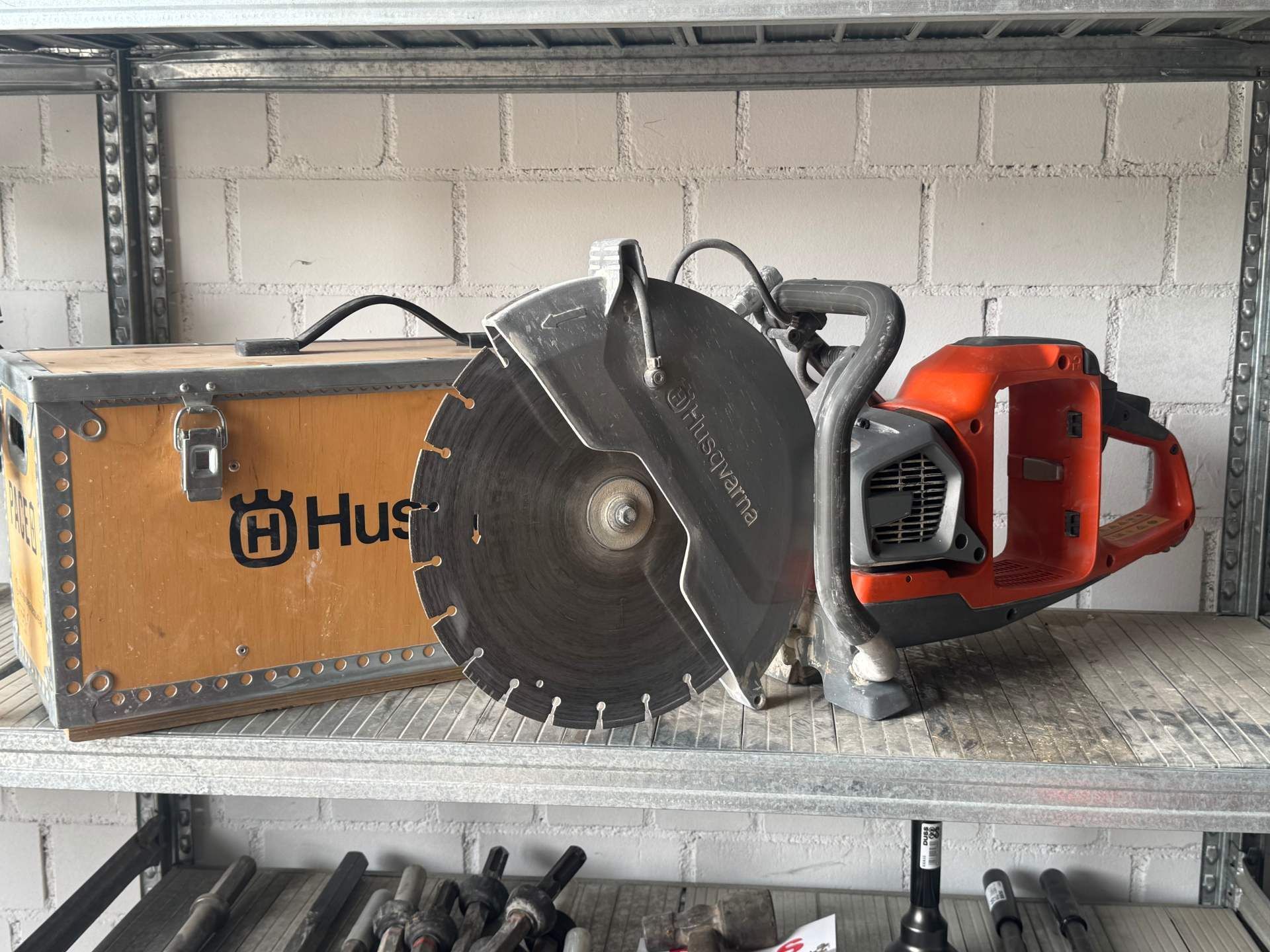 Ein großer orangefarbener Motor-Trennschleifer neben einer Holzkiste im Regal.