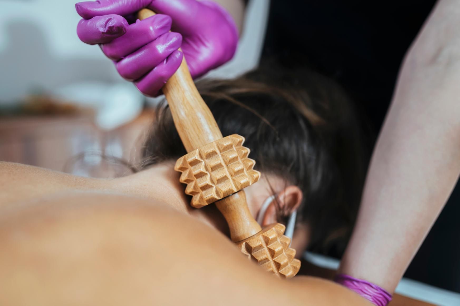 Persona que recibe masaje de espalda con herramienta de madera; manos enguantadas en el marco.