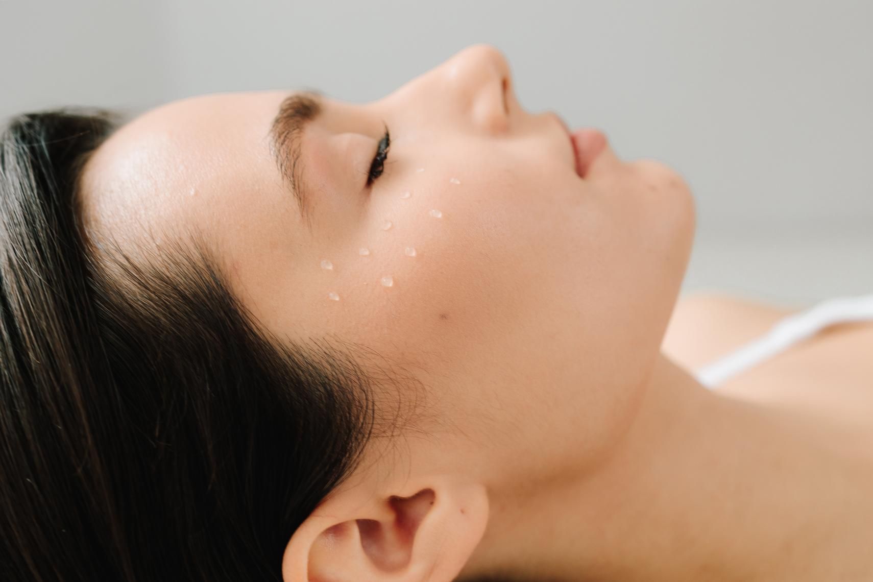 Mujer de cabello oscuro, ojos cerrados, descansando con unas gotas de agua en su rostro.