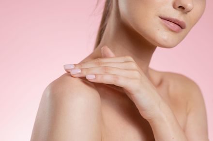 Mujer tocando hombro, piel clara, fondo rosa.