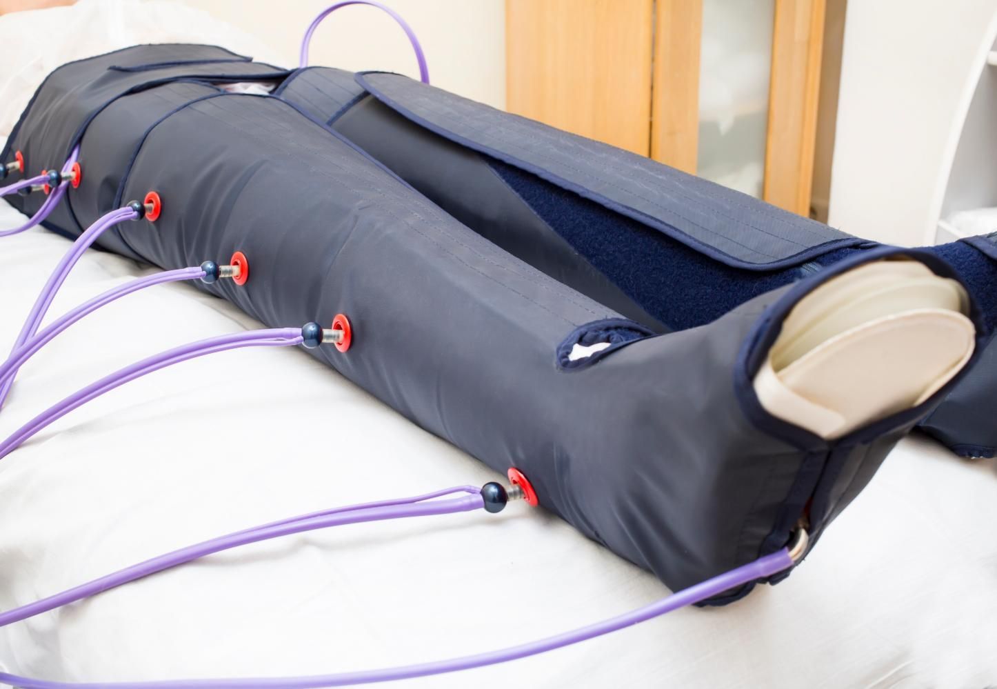 Piernas en un dispositivo de terapia de compresión con tubos de color morado, descansando sobre una cama blanca.