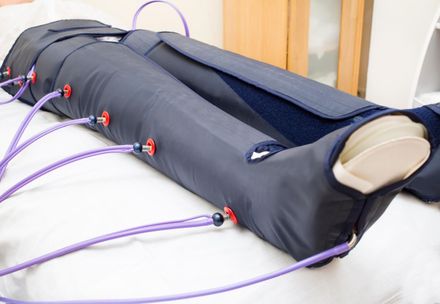 Piernas en un dispositivo de terapia de compresión con tubos de color morado, descansando sobre una cama blanca.