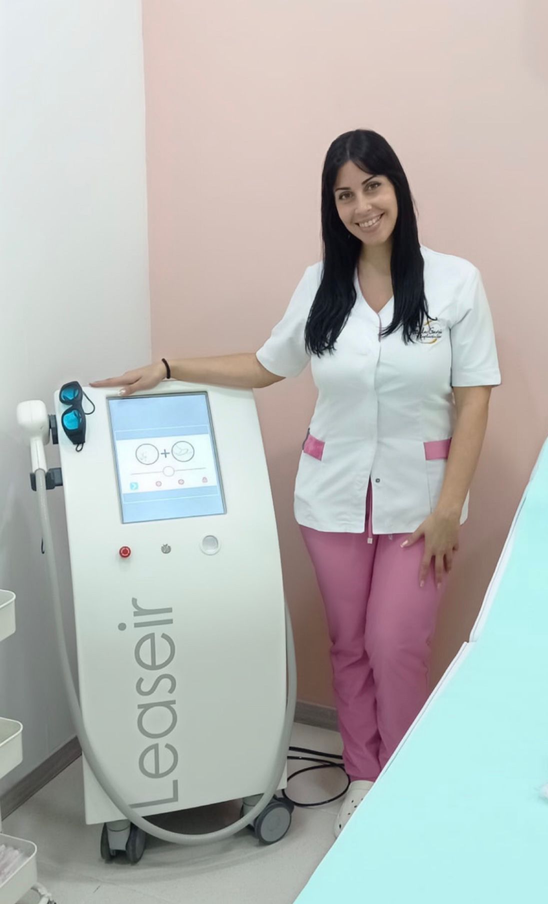 Mujer con uniforme rosa, sonriendo, junto a una máquina de depilación láser Leaseir. Pared rosa claro.
