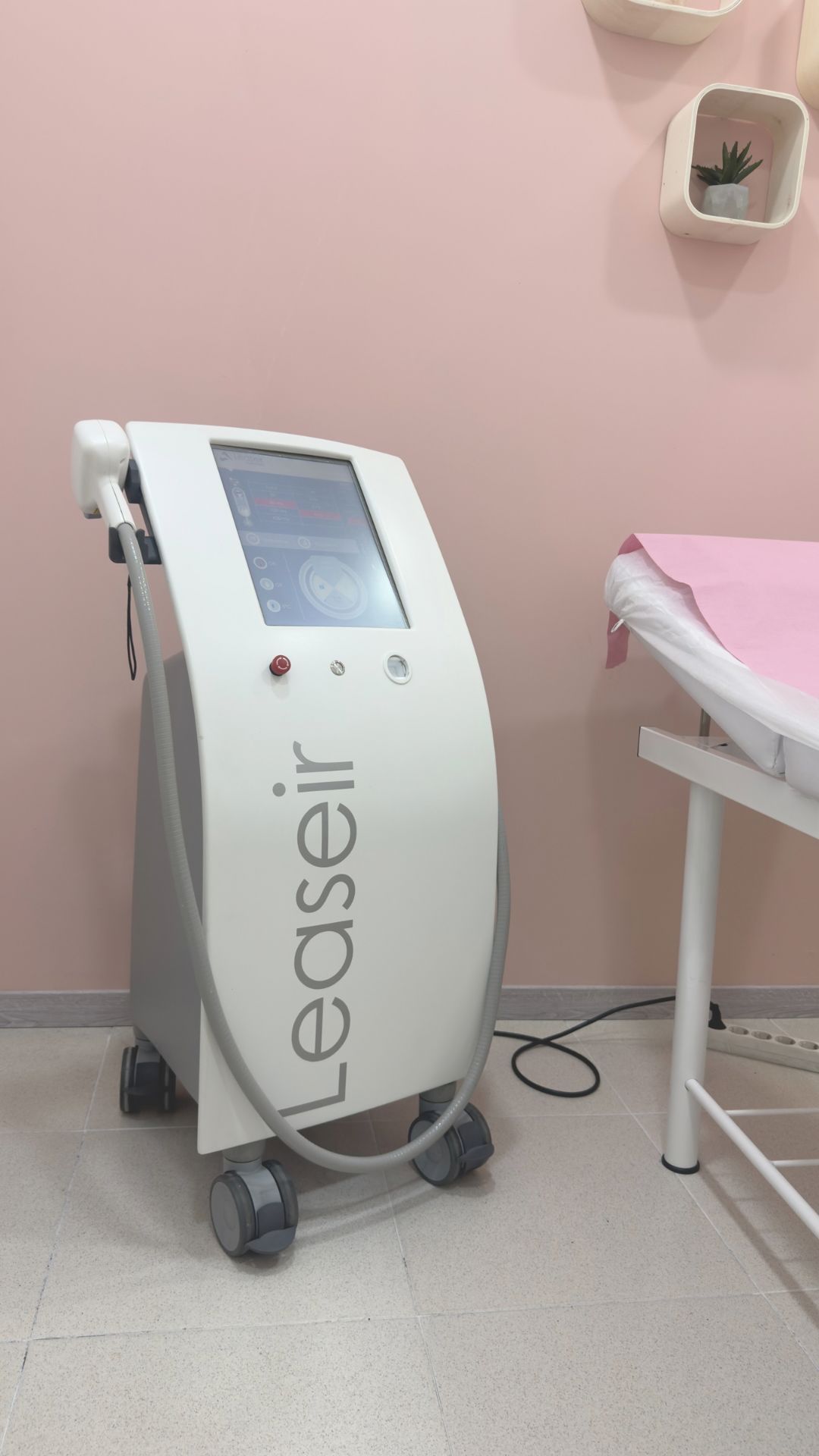 Alquile una máquina de depilación láser en una sala de tratamiento con paredes de color rosa, cerca de una mesa.