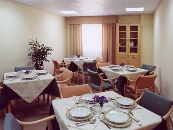 Un comedor con mesas y sillas preparadas para comer.