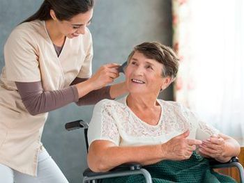 Una anciana en silla de ruedas recibe ayuda de una enfermera.