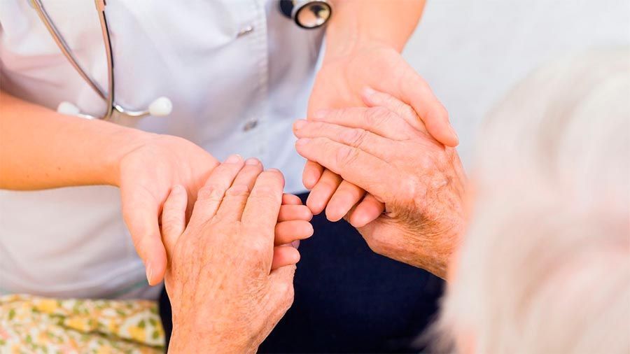 Un médico sostiene las manos de una mujer mayor.