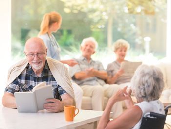 Un grupo de personas mayores están sentadas en una mesa en un hogar de ancianos.