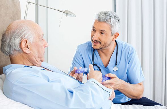 Una enfermera está hablando con un anciano en una cama de hospital.