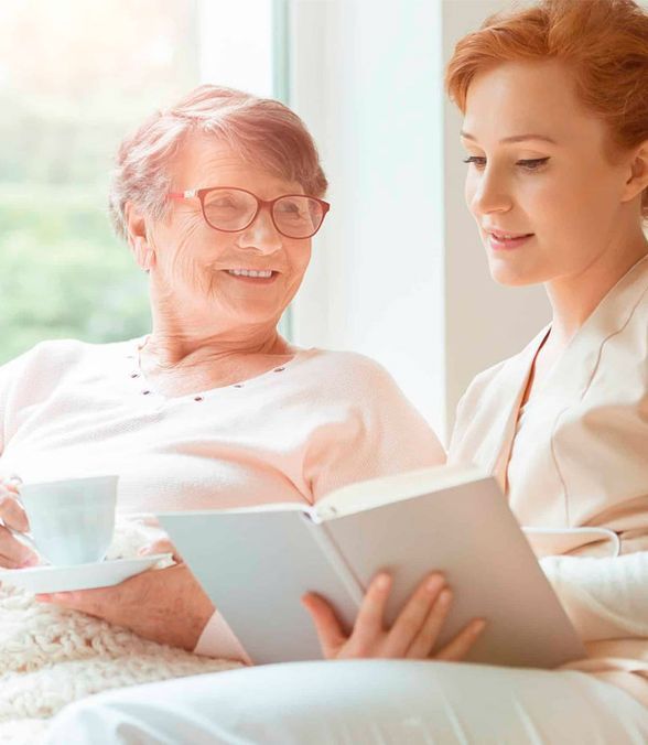 Dos mujeres están sentadas una al lado de la otra leyendo un libro.
