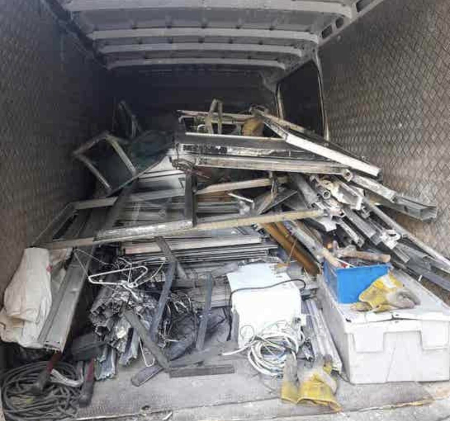 Caja de camioneta repleta de chatarra, cables y contenedores de plástico blanco.