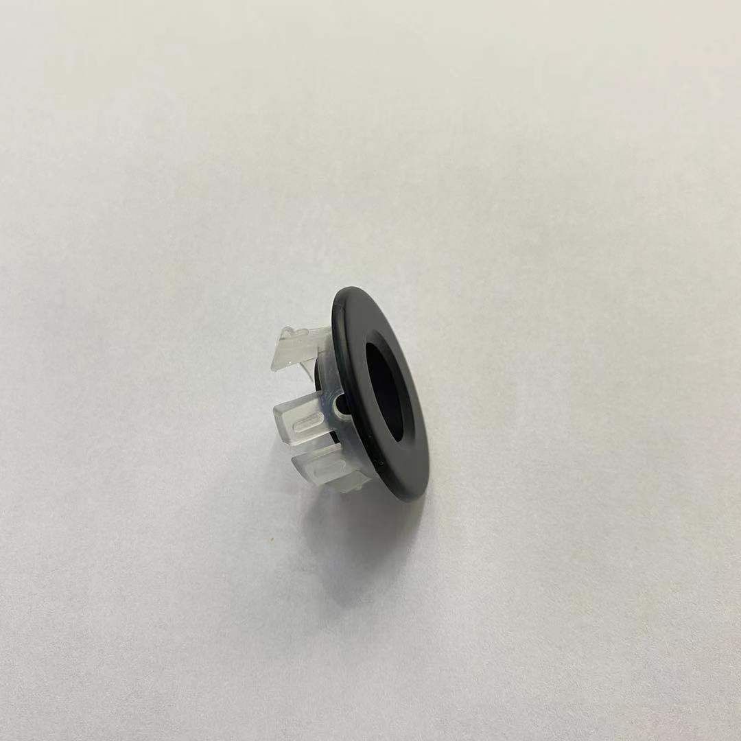 Un pequeño anillo de plástico negro con un agujero en el medio está sobre una superficie blanca.