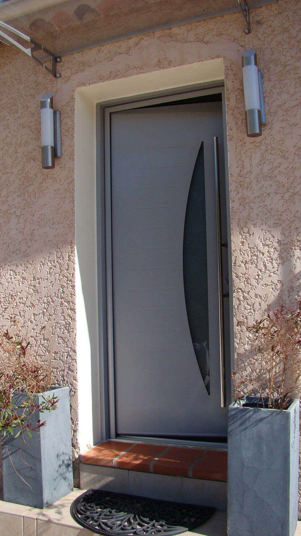 Porte d'entrée grise avec un panneau de verre ovale, flanqué de deux appliques murales, sur un mur rose moucheté.
