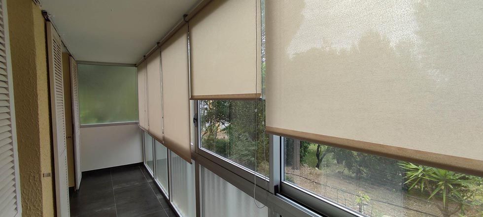 Un balcon étroit avec stores fermés, donnant sur les arbres et la verdure.