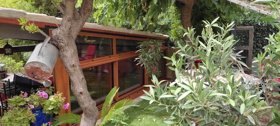 Une structure à ossature bois avec de grandes fenêtres dans un jardin luxuriant, avec un arbre.