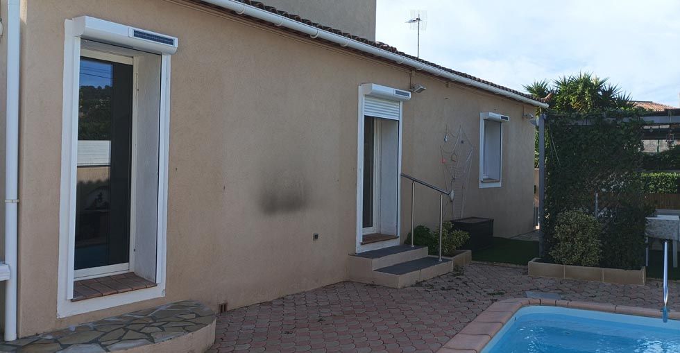 Extérieur de maison beige avec fenêtres et porte, une piscine et une cour en gravier.