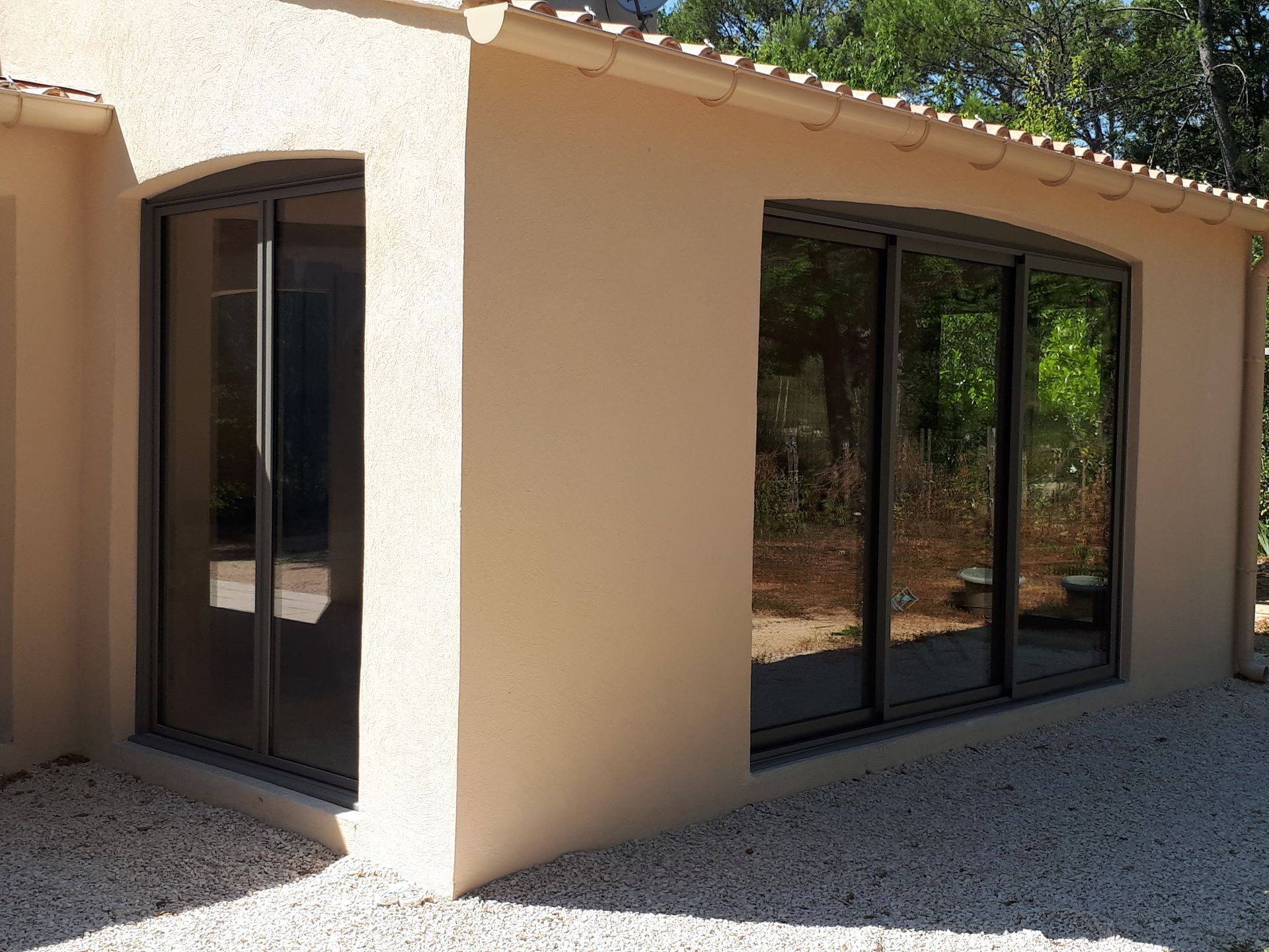 Bâtiment en stuc beige avec de grandes baies vitrées et un sol en gravier.