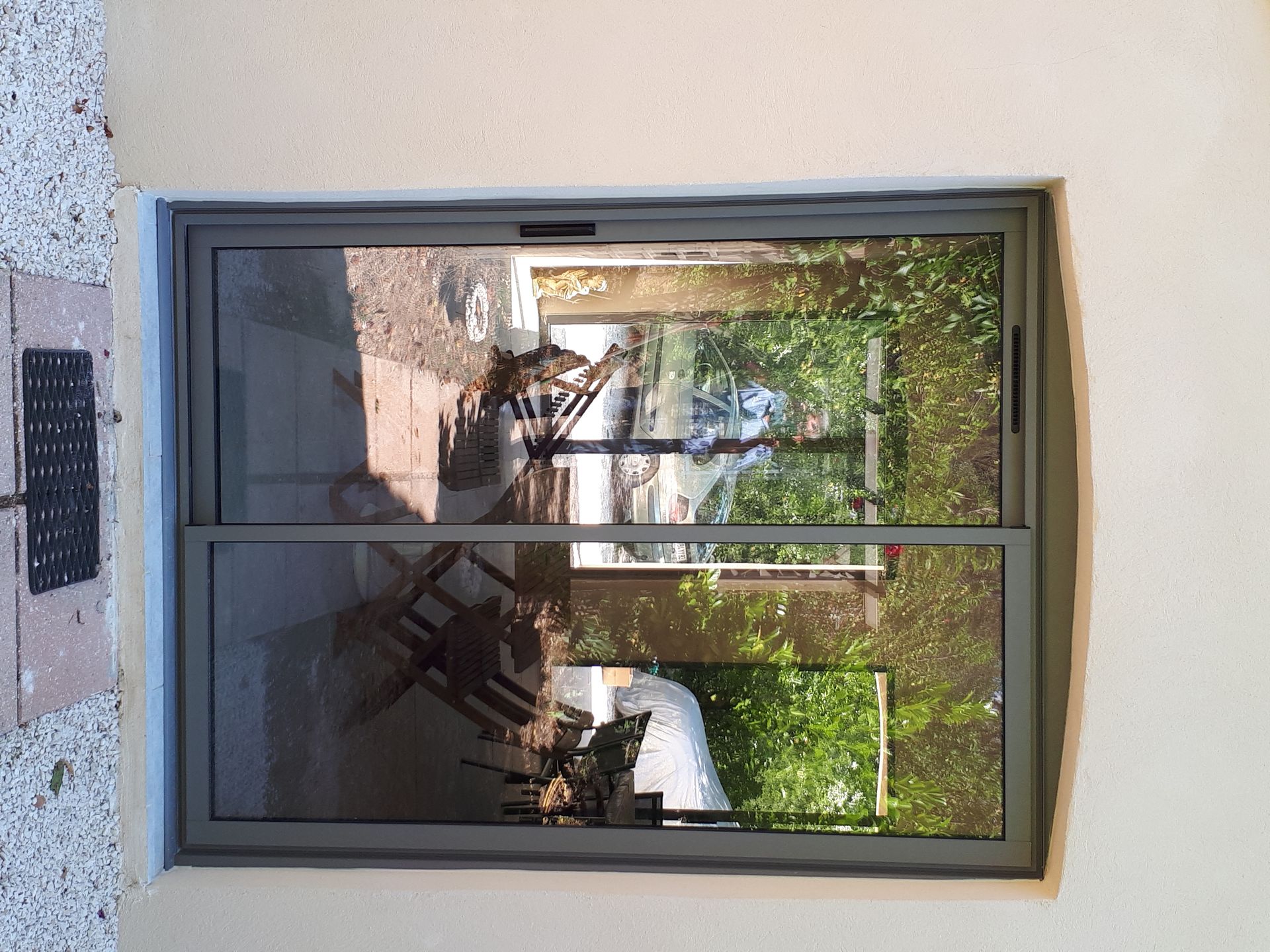 Porte coulissante en verre à cadre gris avec reflet de mobilier d'extérieur et de verdure.