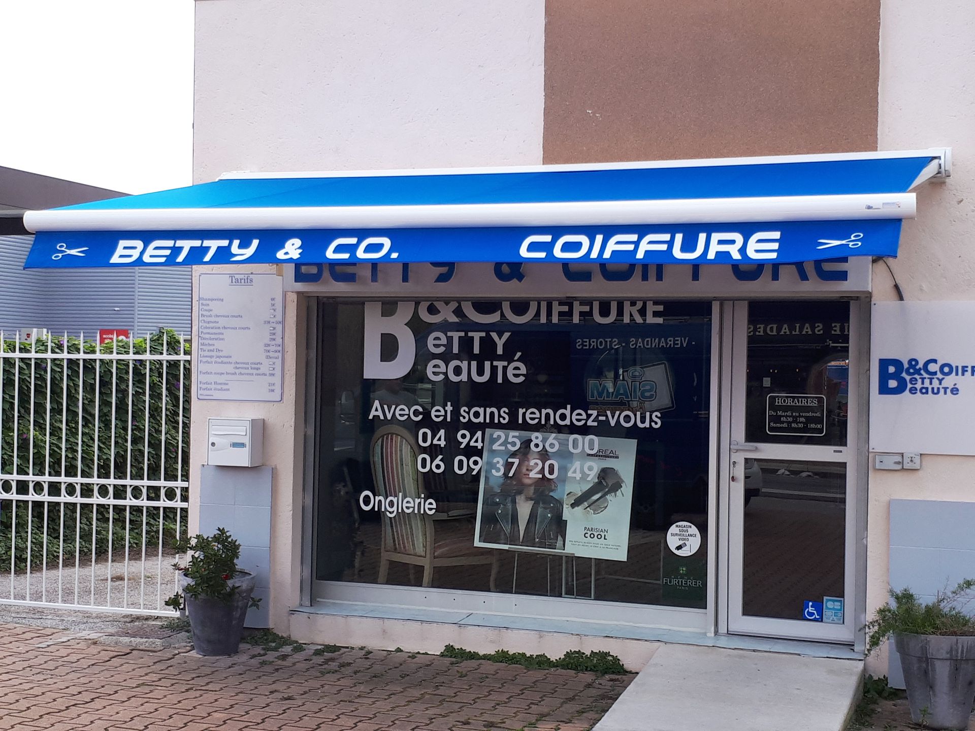 Une devanture pour « Betty & Co. Coiffure » avec auvent bleu, porte vitrée et enseigne.