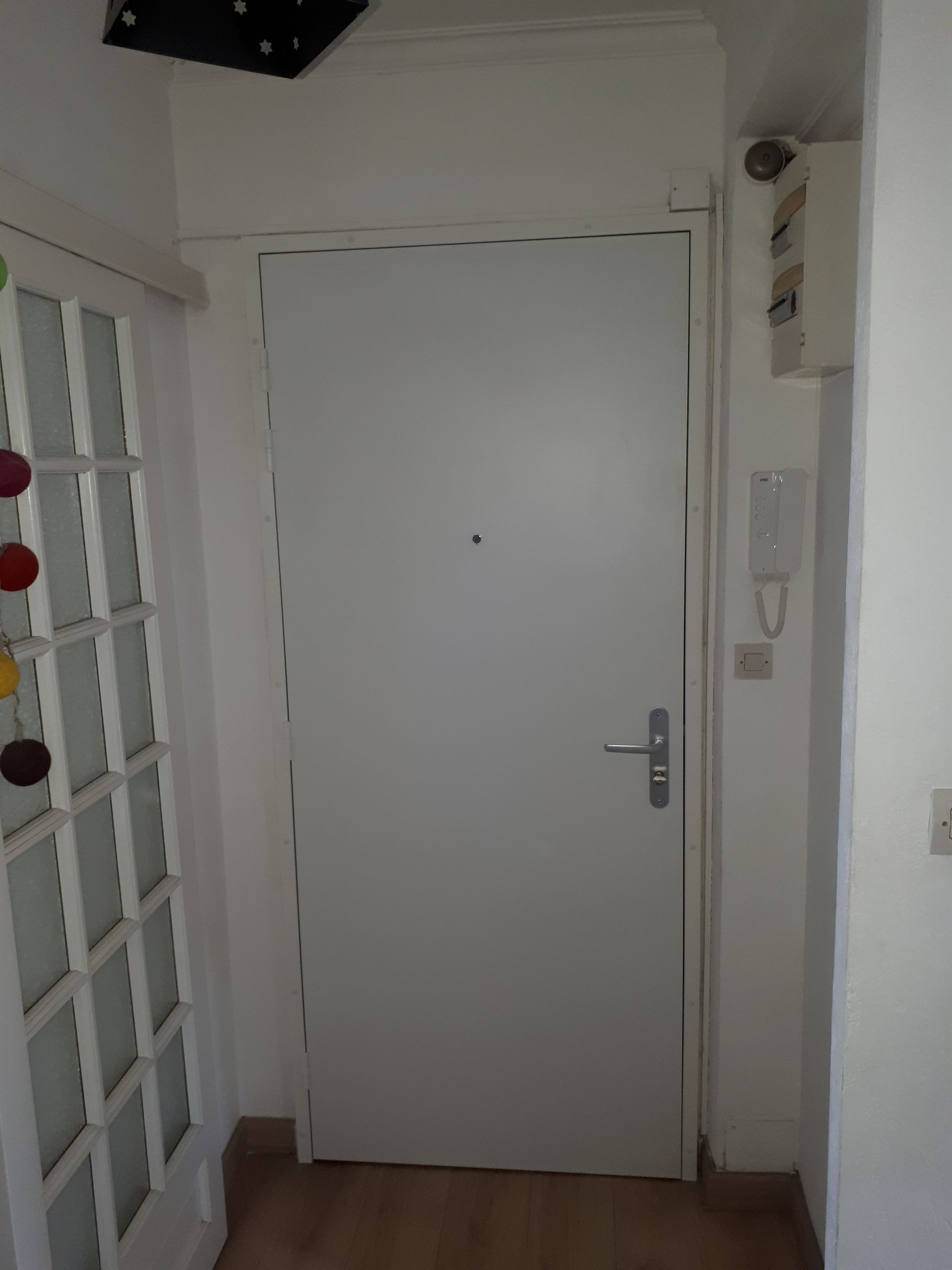 Porte intérieure blanche avec judas, poignée en métal et interphone sur le côté droit du cadre.