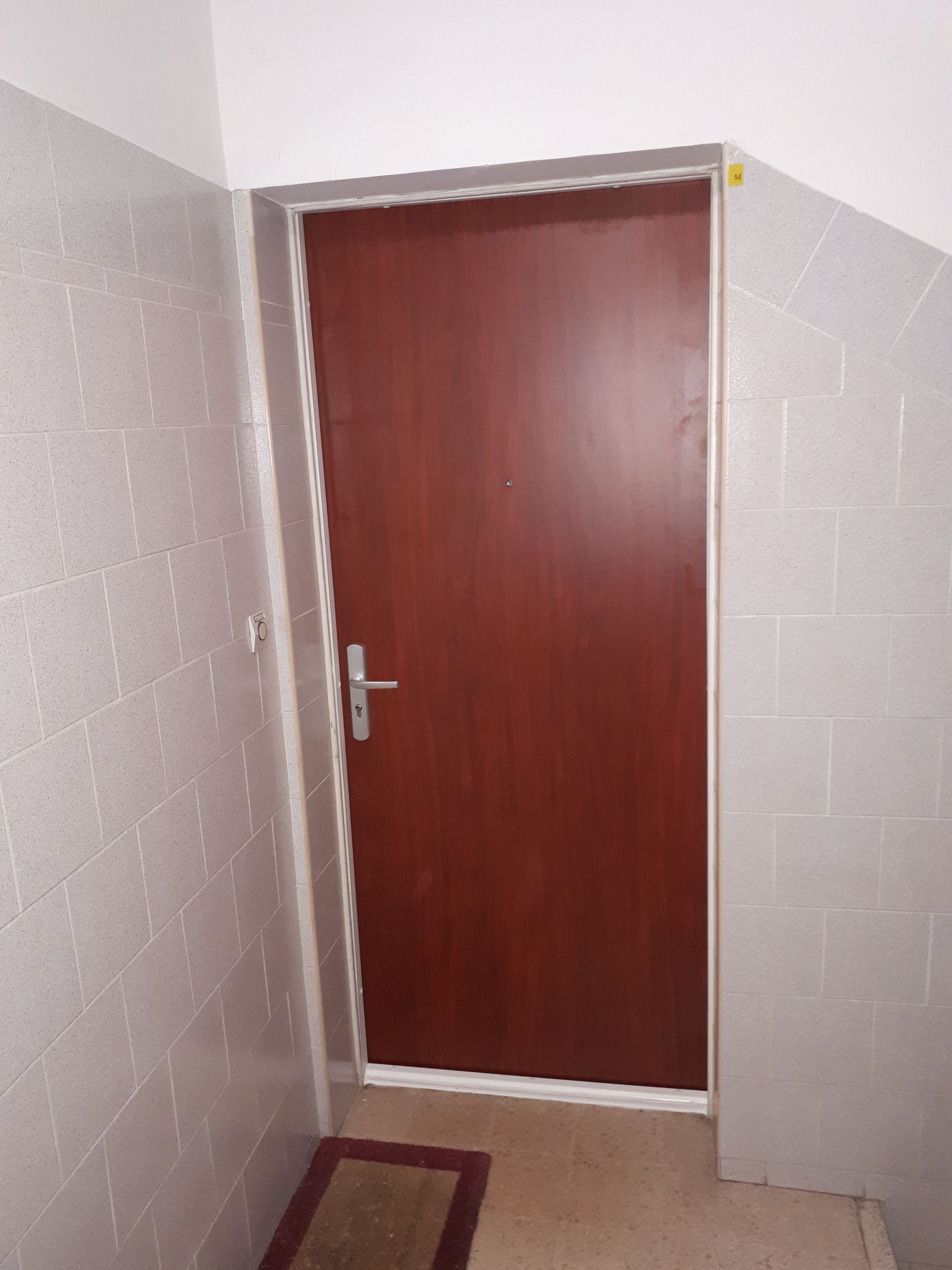 Porte marron dans un couloir carrelé avec un petit paillasson.