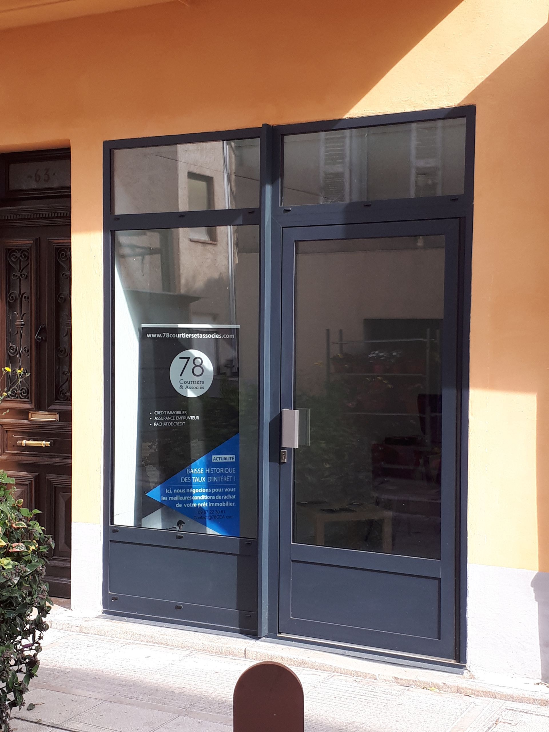 Porte et fenêtre en métal gris sur un bâtiment orange, un panneau bleu visible à l'intérieur.