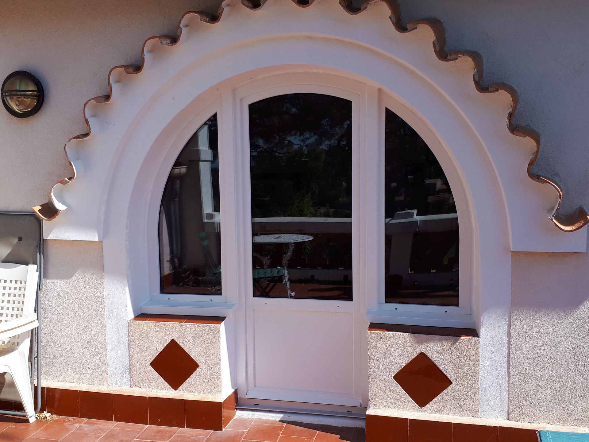 Porte blanche avec cadre arqué et fenêtres latérales. Garnitures décoratives. Finitions marron sur stuc extérieur.