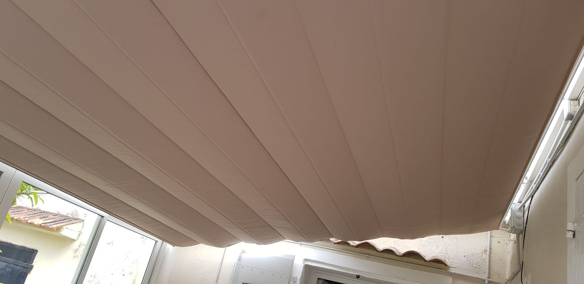 Store rétractable beige au dessus d'un patio avec vue sur une fenêtre.