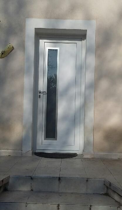 Porte blanche avec un long panneau de fenêtre, entouré d'un cadre blanc, sur un bâtiment de couleur claire avec des marches qui y mènent.