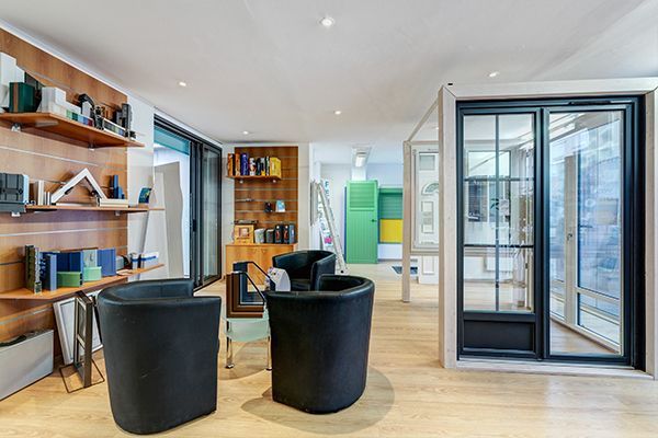 Intérieur d'une salle d'exposition avec sièges et vitrines. Parquet en bois clair, chaises noires et étagères avec échantillons.