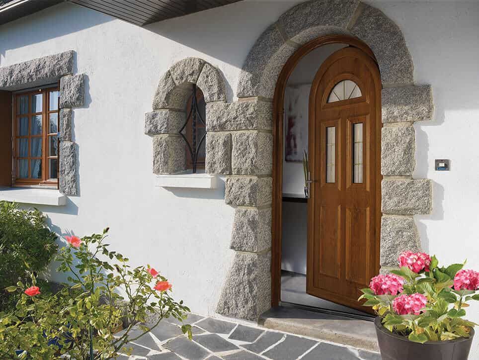 Porte en pierre cintrée et cadre de fenêtre d'une porte en bois sur une maison blanche.