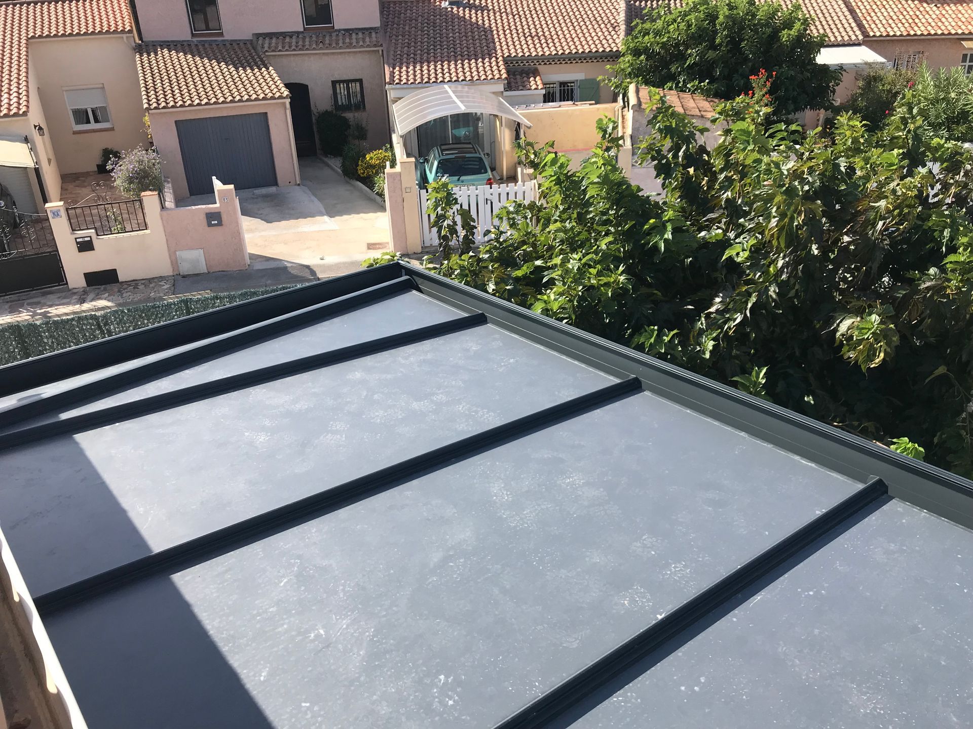 Un toit plat et gris avec des coutures noires ; quartier résidentiel en arrière-plan.