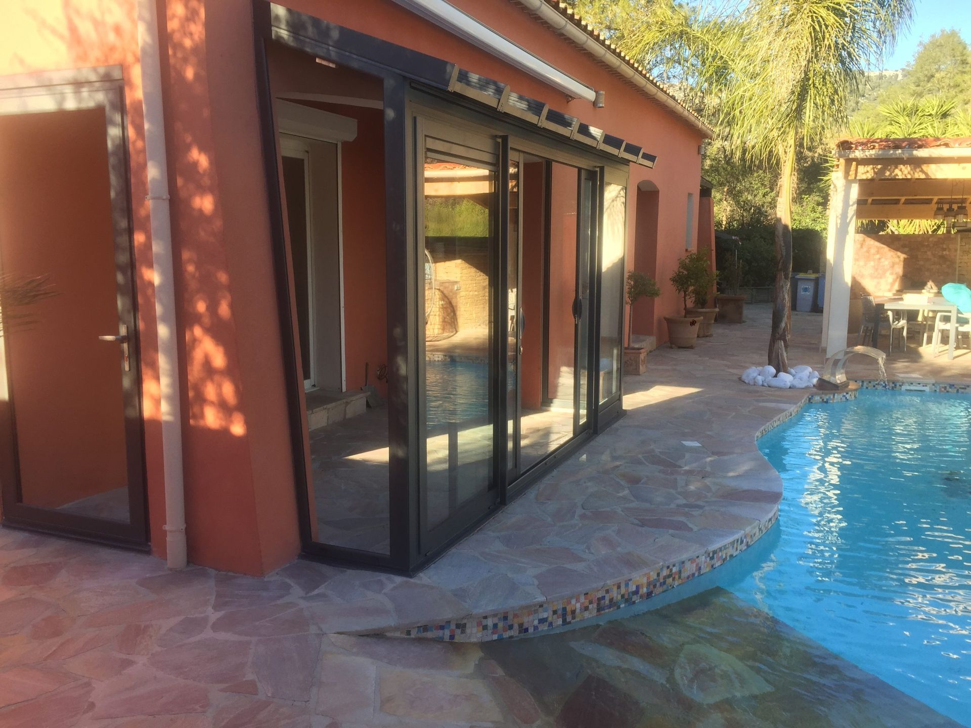 Au bord de la piscine avec portes coulissantes en verre, bâtiment rouge, eau de piscine bleue et patio en pierre.
