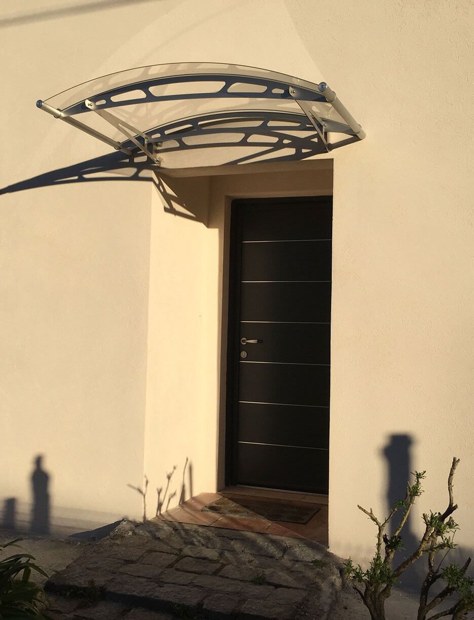 Porte noire avec auvent. Ombres de plantes et d'une personne projetées sur le mur blanc.