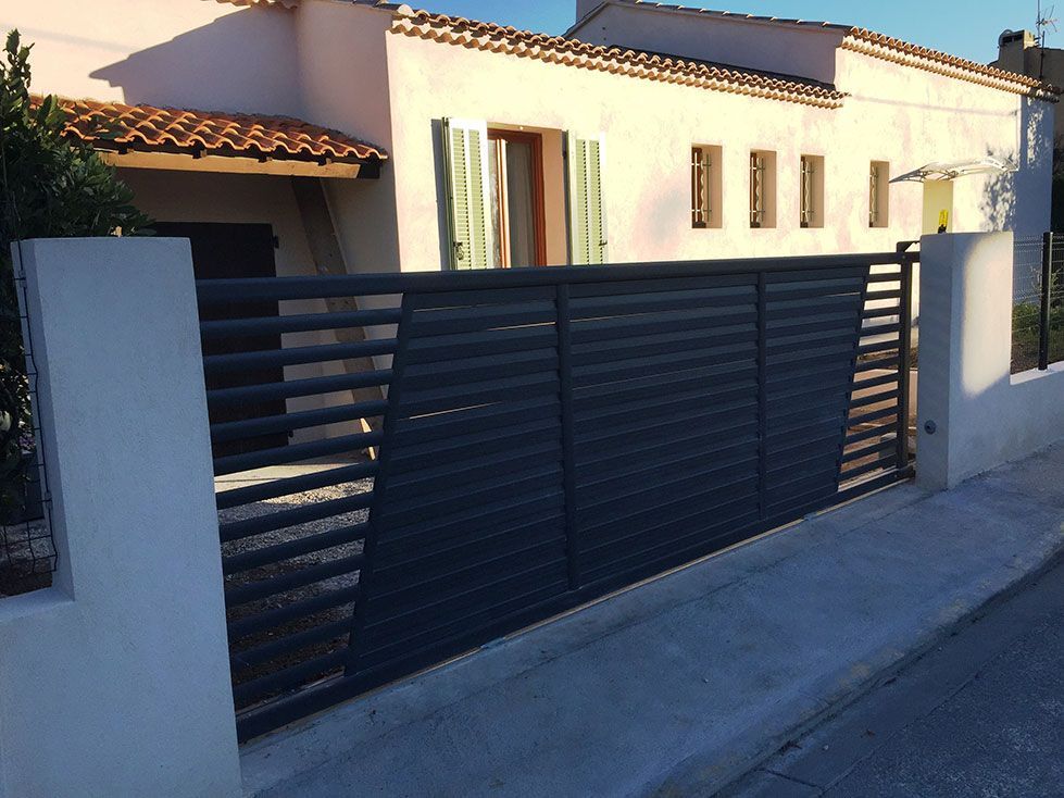 Portail en métal gris devant une maison blanche au toit en terre cuite.