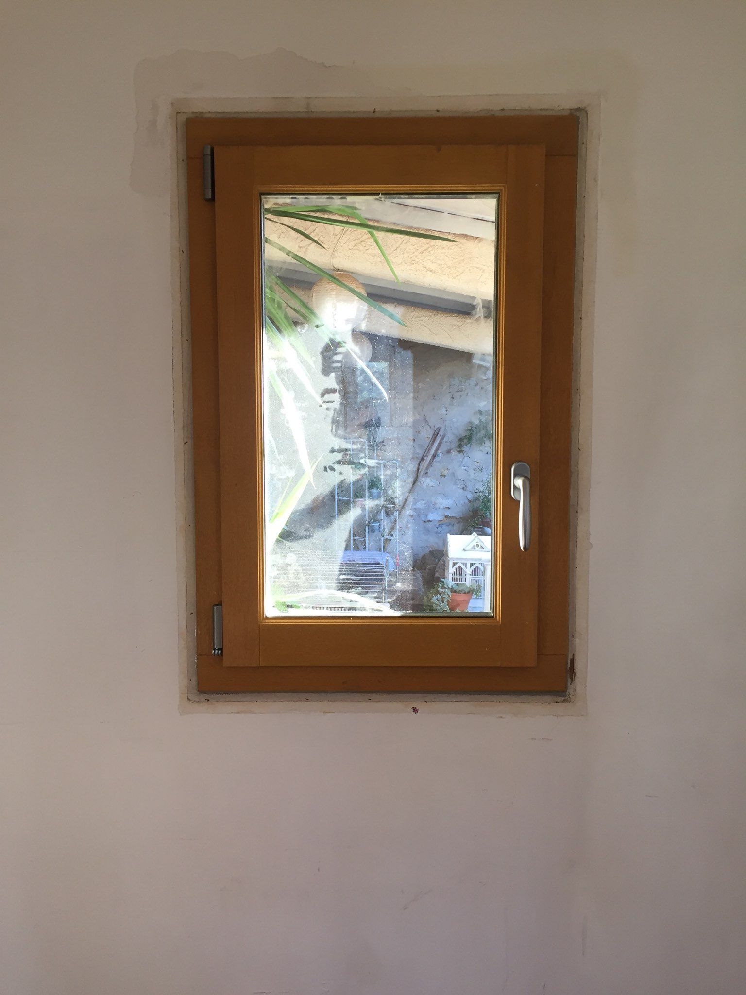 Fenêtre à cadre en bois dans un mur blanc, montrant une vue extérieure floue.