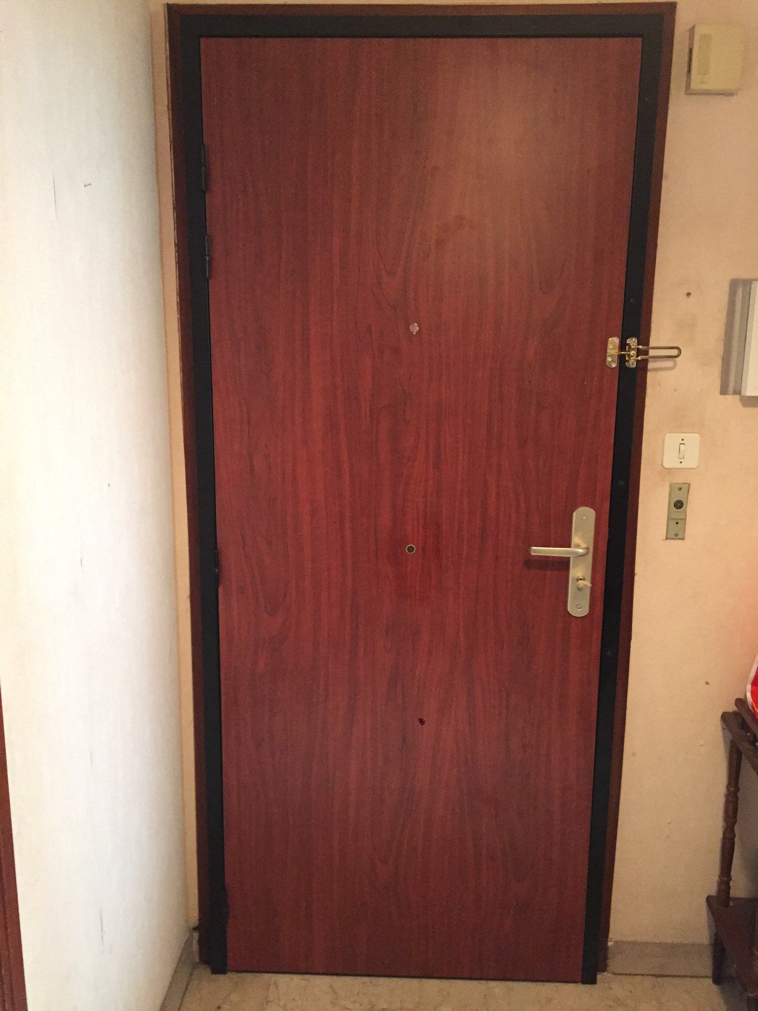 Porte en bois avec grain brun, cadre noir, quincaillerie en métal et murs de couleur claire dans un décor intérieur.