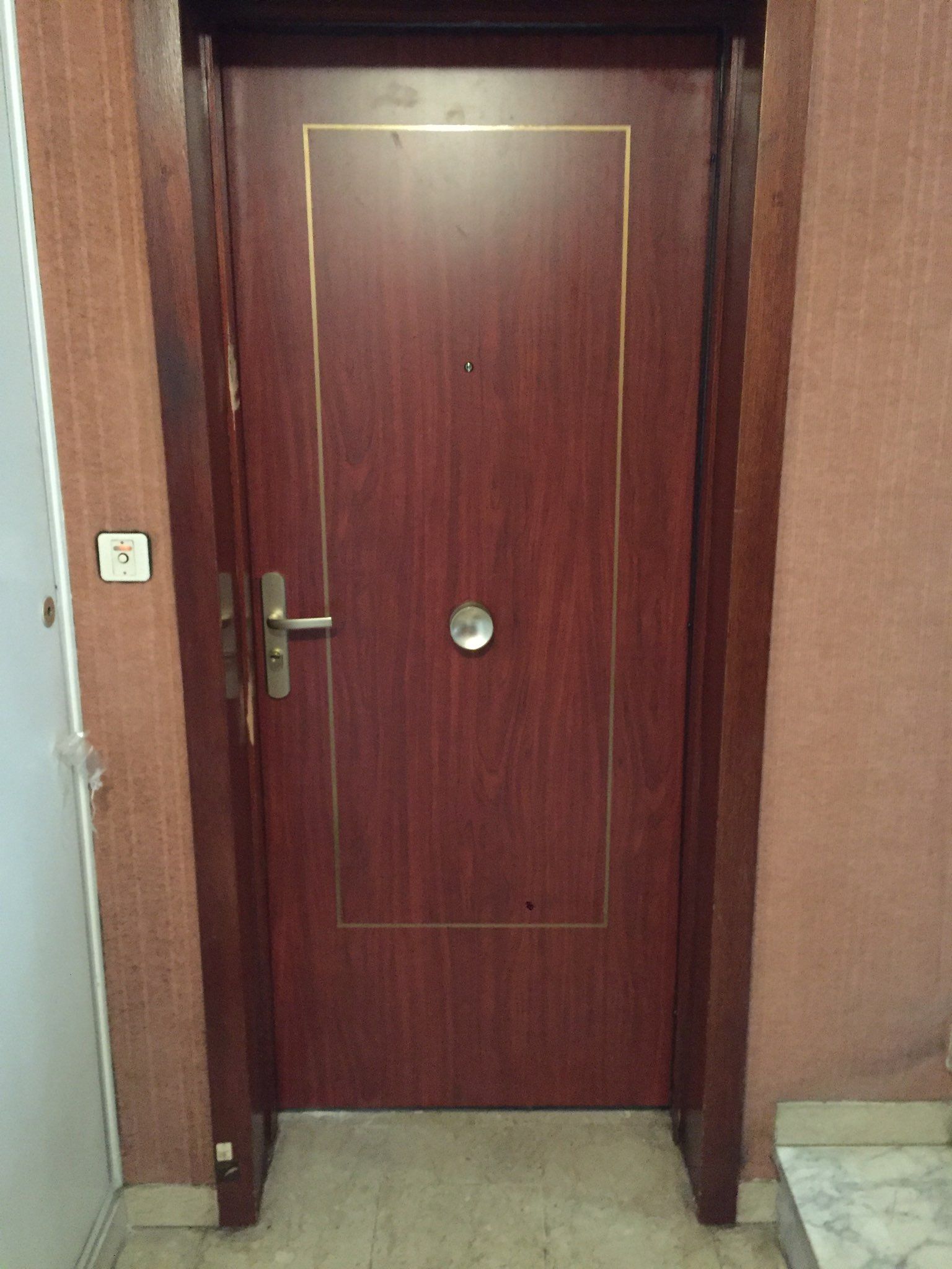 Porte en bois marron avec garniture dorée, poignée et judas argentés.