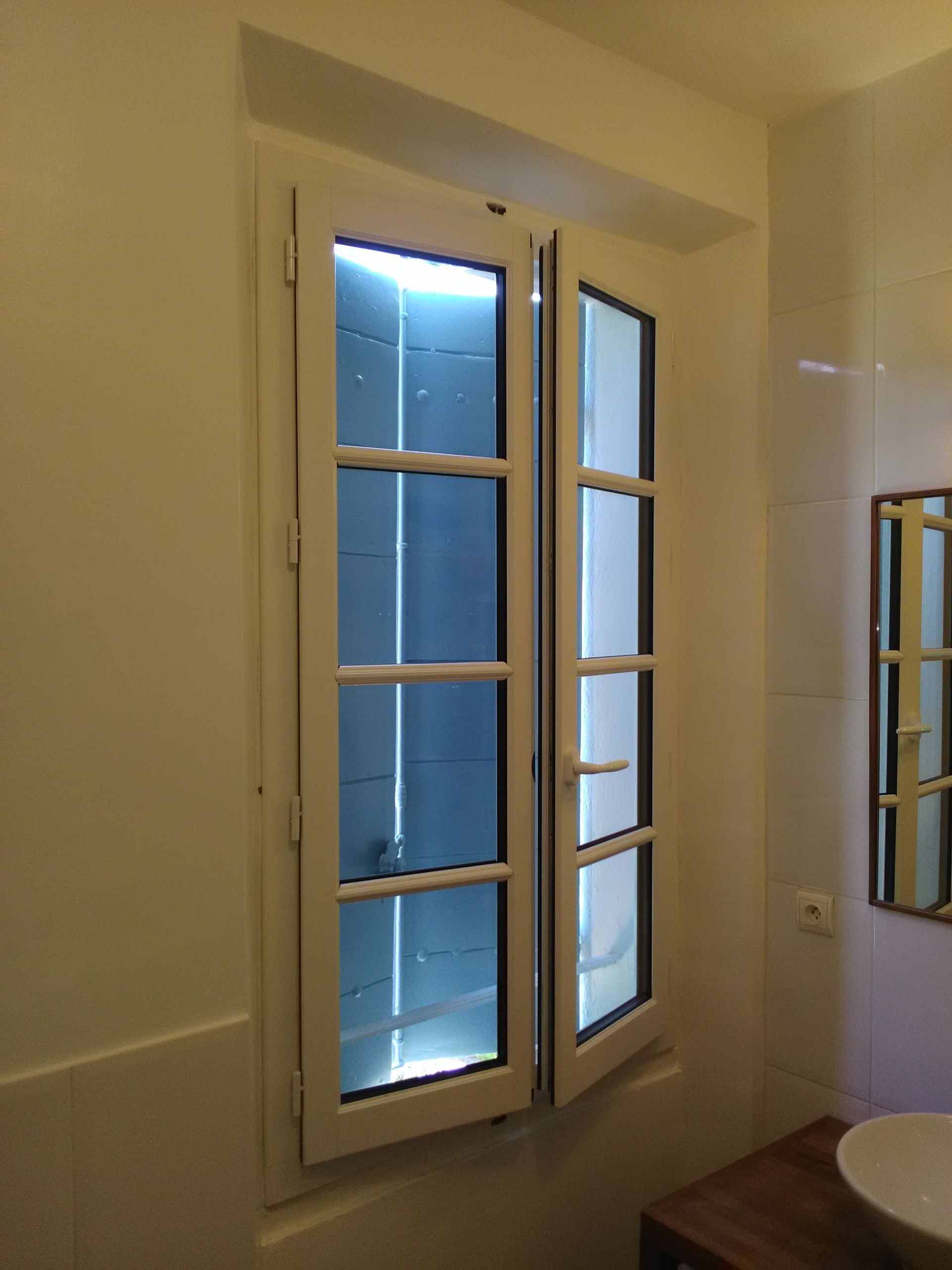 Fenêtre blanche, ouverte d'un côté, dans une salle de bain aux murs blancs.