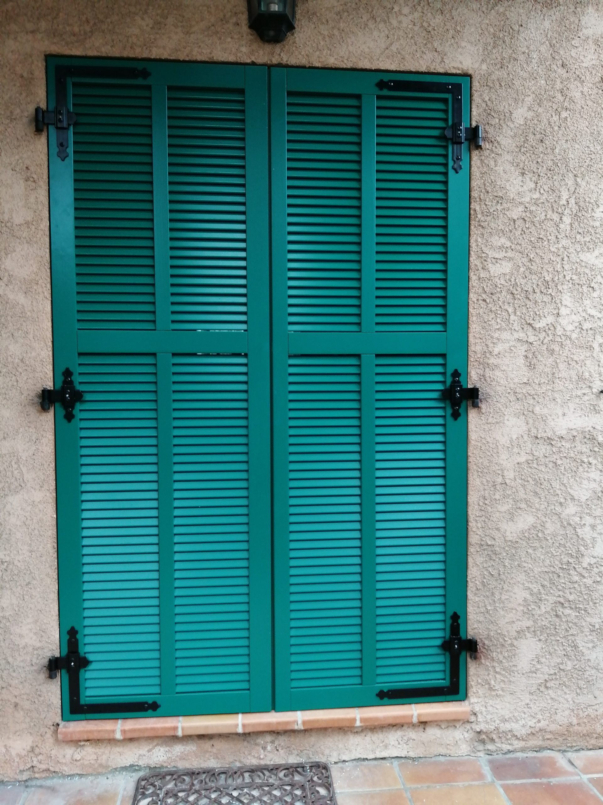 Portes à volets verts sur un bâtiment en stuc avec quincaillerie noire.