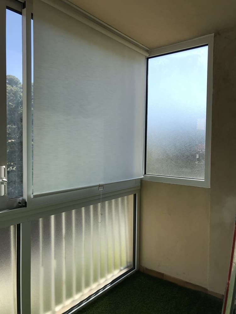 Balcon d'angle avec fenêtre en verre dépoli et store partiellement tiré.