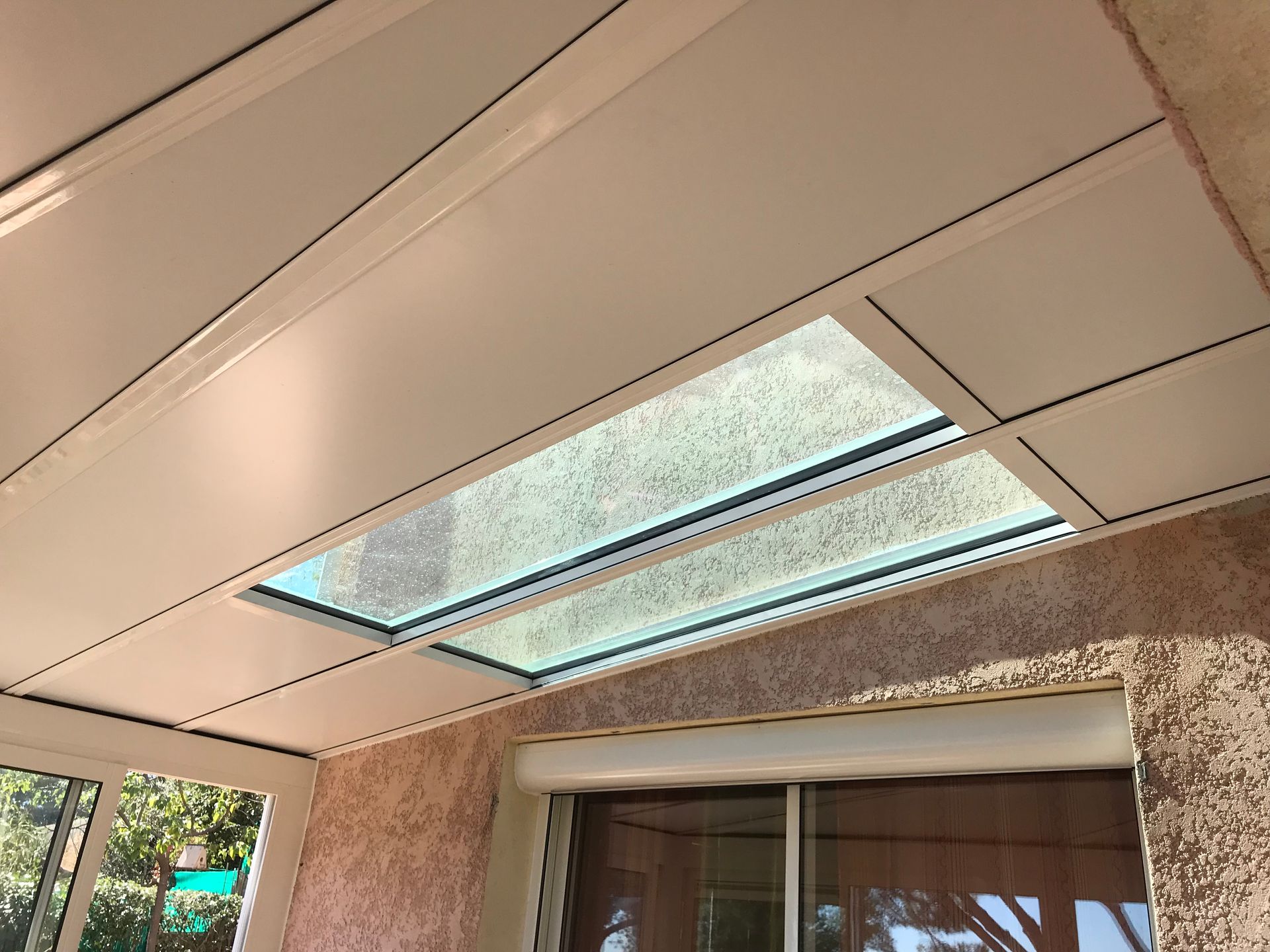 Toiture blanche et vitrée avec puits de lumière au dessus d'un patio avec murs en stuc et fenêtre fermée.