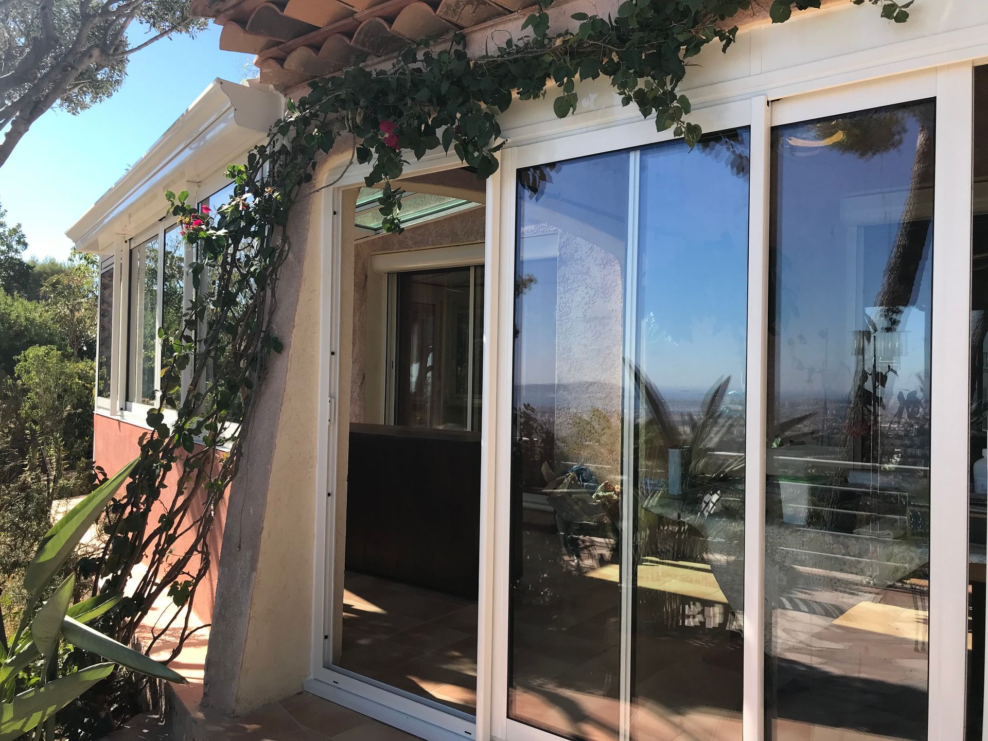 Extérieur d'un bâtiment avec portes coulissantes en verre, vignes et vue sur le paysage environnant.