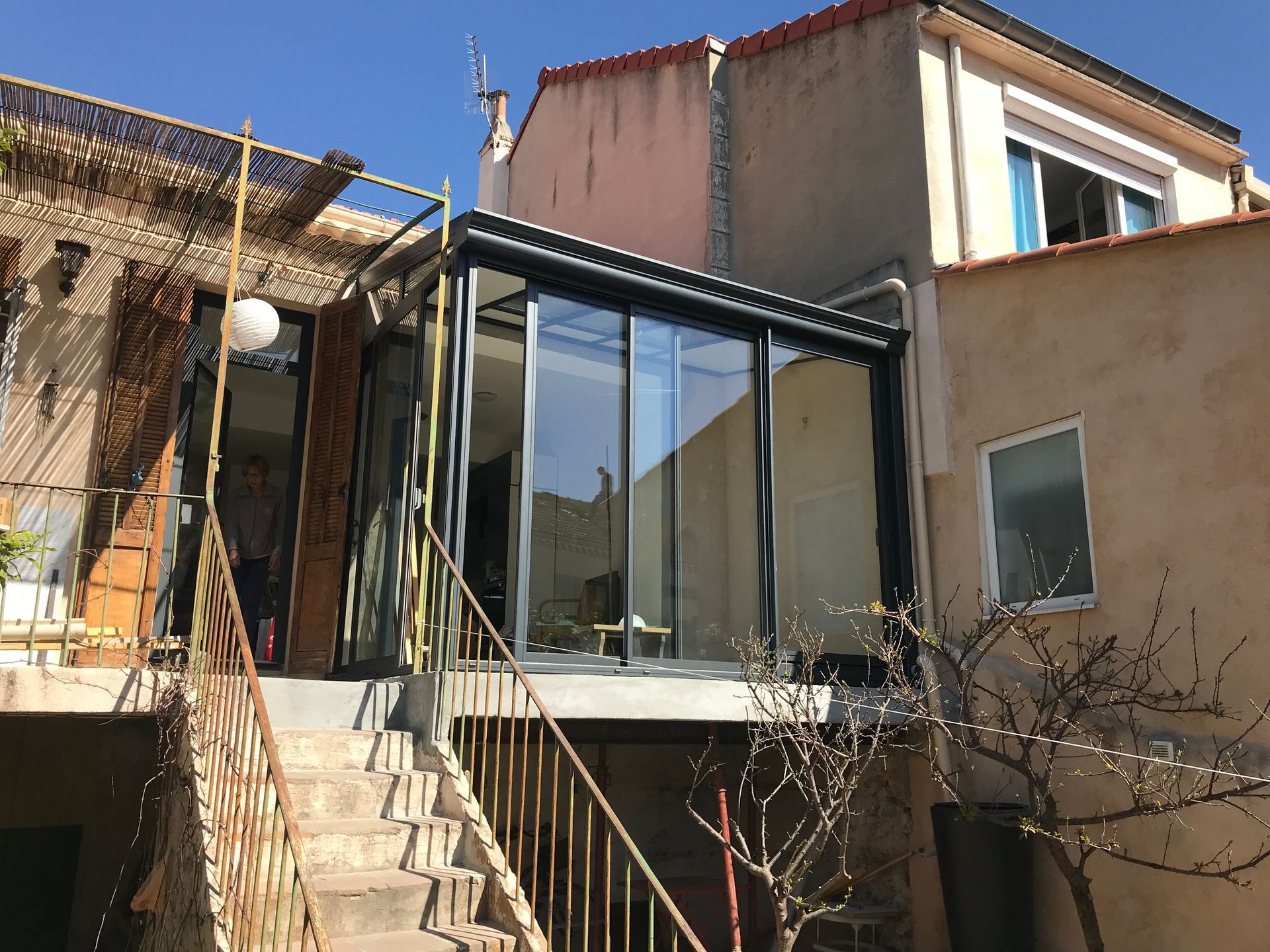 Véranda avec portes coulissantes en verre sur une plate-forme surélevée, reliée par des escaliers.