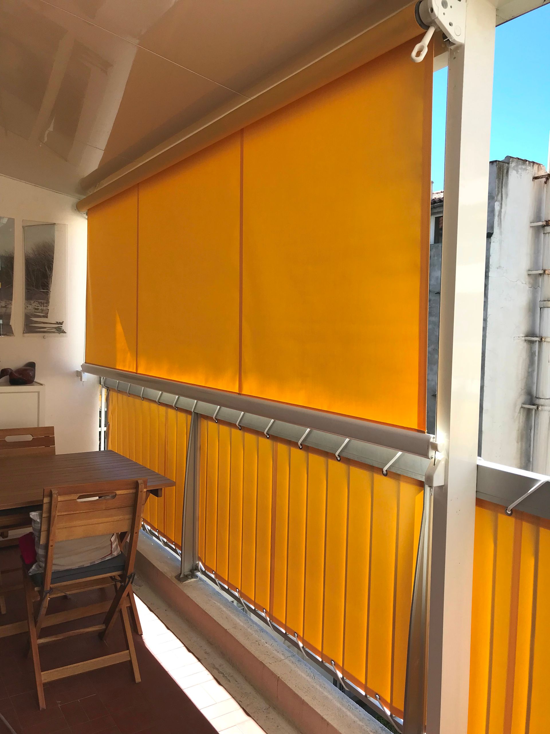 Stores enrouleurs extérieurs jaunes, partiellement abaissés, sur un balcon.