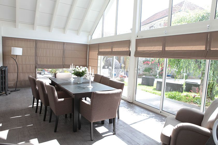 Salle à manger avec grandes fenêtres, longue table dressée pour plusieurs personnes, tons neutres.