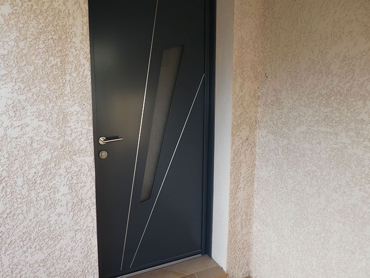 Porte d'entrée gris foncé avec panneau de verre incliné et lignes d'accent argentées dans une porte en stuc beige.