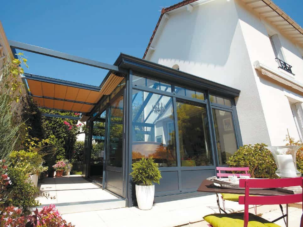 Ajout d'une véranda en verre à une maison blanche avec un auvent rétractable et des meubles de patio.