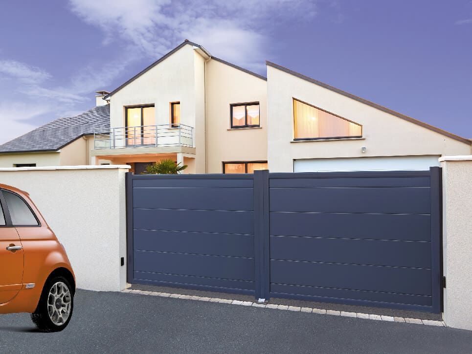 Un portail coulissant bleu devant une maison moderne, une petite voiture orange garée sur la gauche.