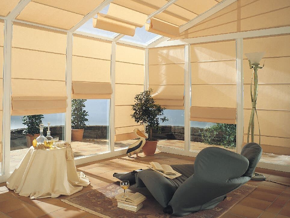 Véranda avec stores beiges, une personne dans un fauteuil inclinable, vue sur l'océan.